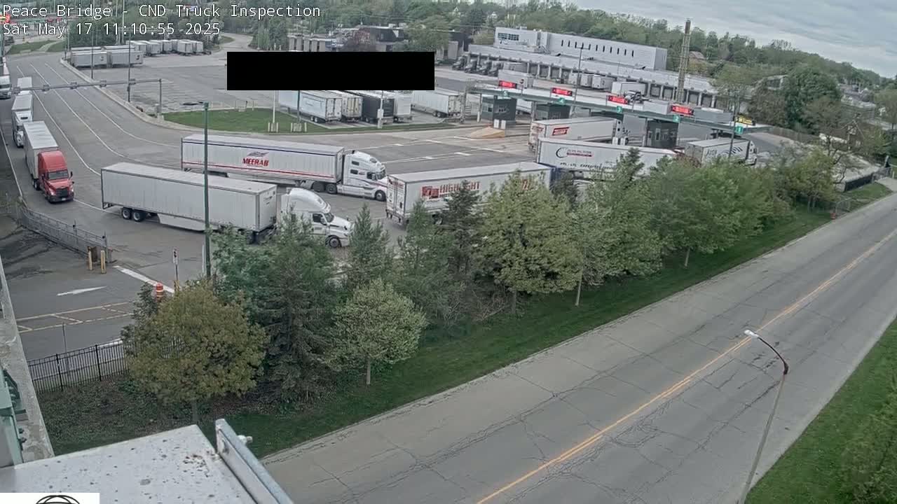 Several semi-trailer trucks are parked and moving at a truck inspection station on an overcast day.