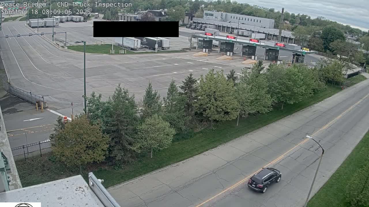 An overhead view shows a mostly empty truck inspection area with a dark-colored SUV driving on a nearby road under an overcast sky.