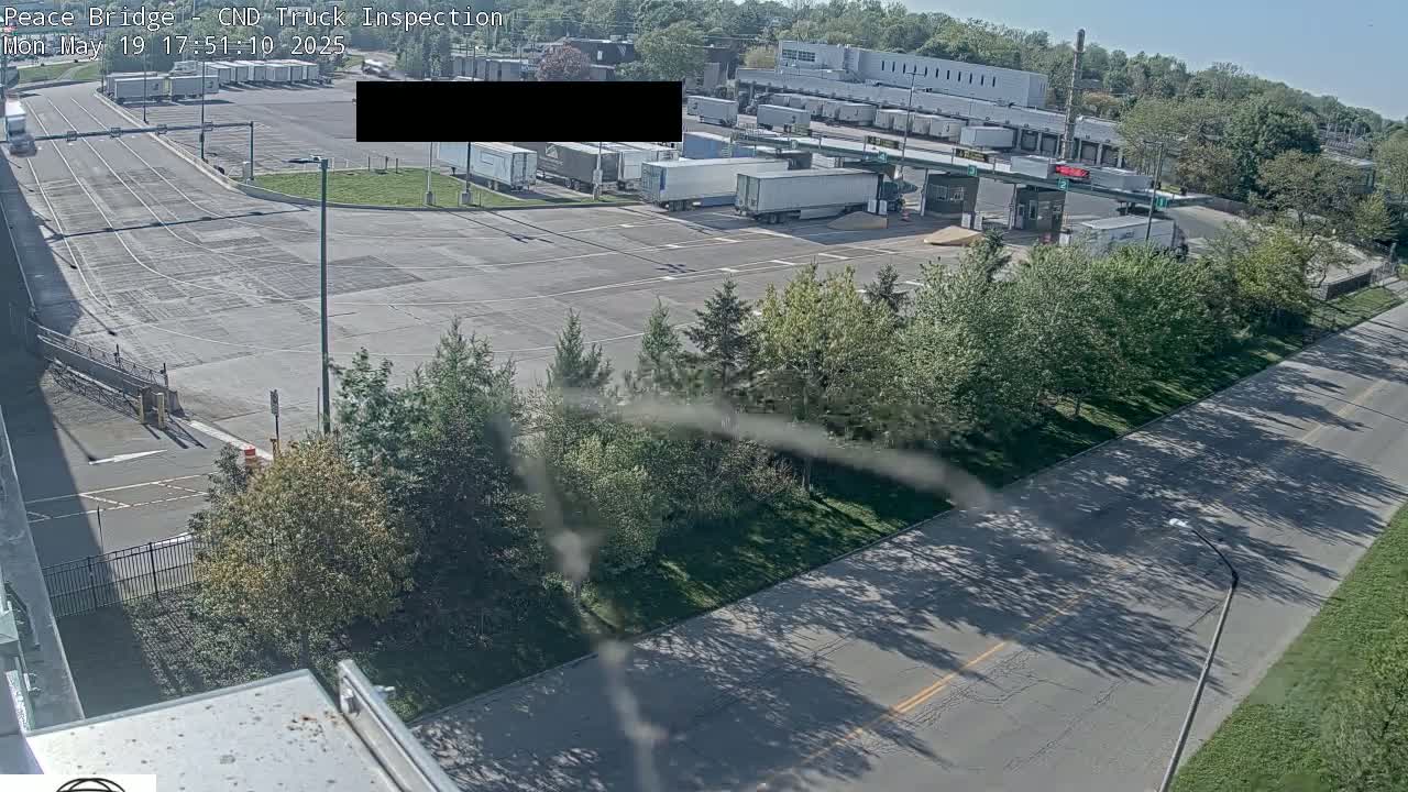 A high-angle, sunny-day view of a truck inspection station with numerous semi-trailers parked in a large paved lot, surrounded by trees and roads.