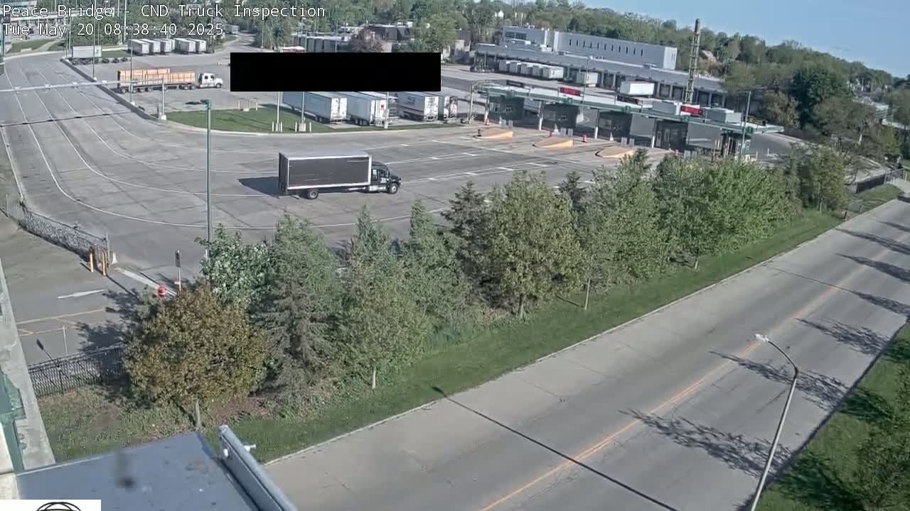 A truck inspection station with several trucks and trailers, surrounded by trees and roads, on a sunny day.