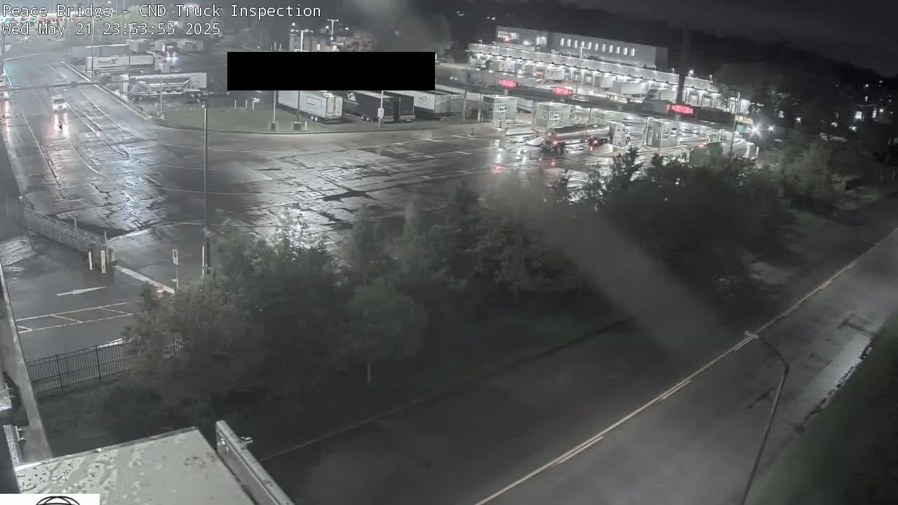 A nighttime, wet roadway scene shows a truck inspection area with several vehicles present under dim lighting.