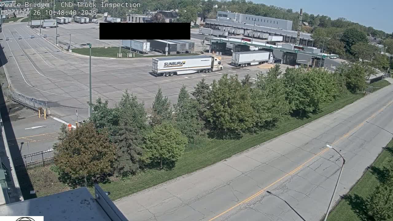 A truck inspection area with several semi-trucks parked on a sunny day, surrounded by trees and a roadway.