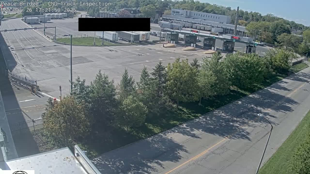 An aerial view of a truck inspection station on a sunny day, showing several trucks parked near inspection booths and surrounded by green trees and a roadway.