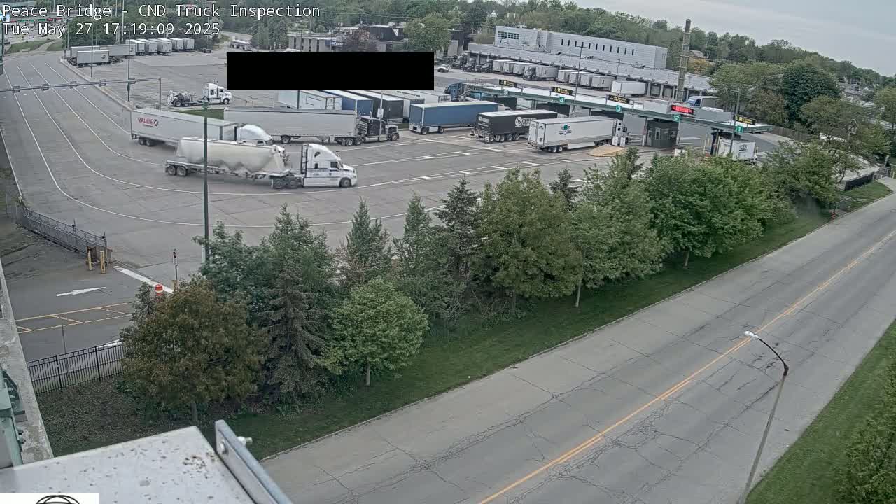 An aerial view shows a truck inspection area with numerous semi-trucks in a parking lot on a partly sunny day.