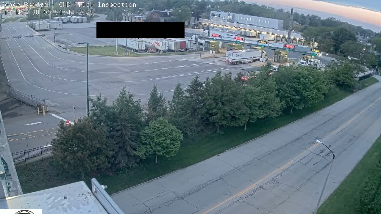 An aerial view shows a truck inspection station with several semi-trucks and cars at dusk under a partly cloudy sky.
