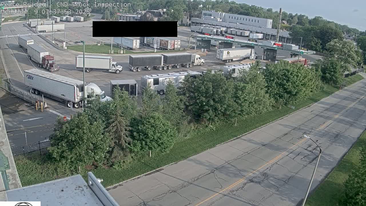A truck inspection area with numerous semi-trucks and trailers parked and moving under a mostly sunny sky.