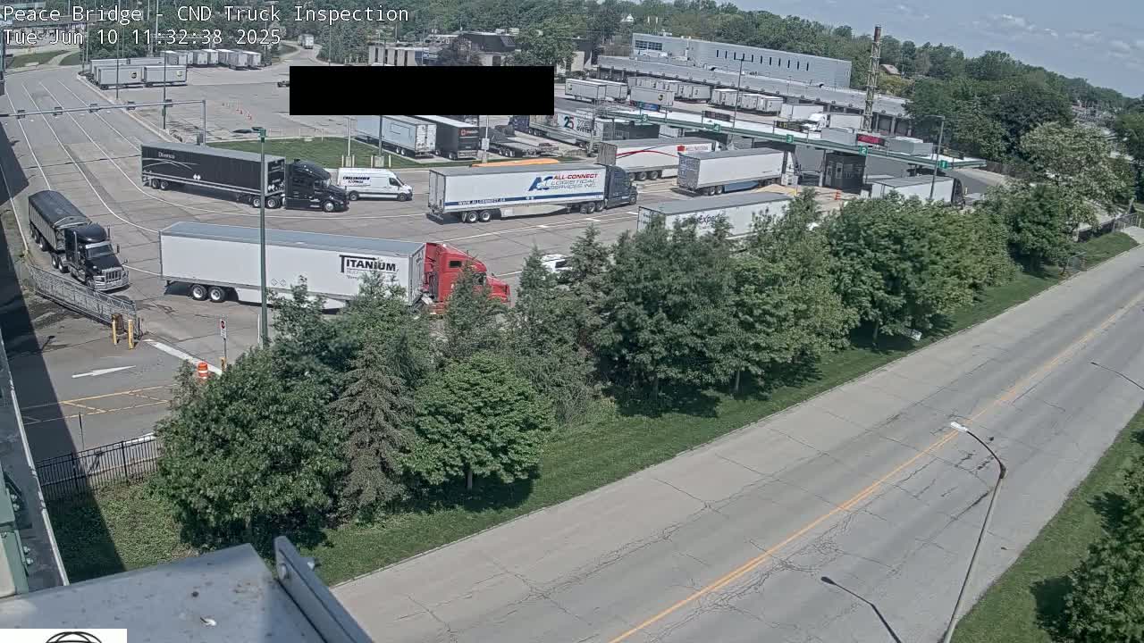 A truck inspection area with numerous semi-trucks and other vehicles parked and moving under a partly sunny sky.