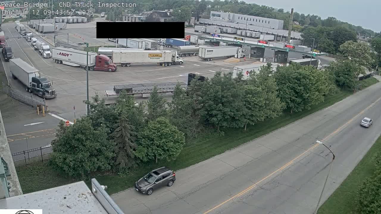 An aerial view shows a truck inspection area with numerous semi-trucks and a few cars, under an overcast sky.