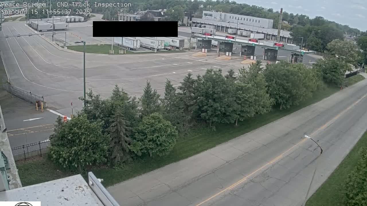 An aerial view of a truck inspection station with several trucks, surrounded by trees and a road under overcast skies.