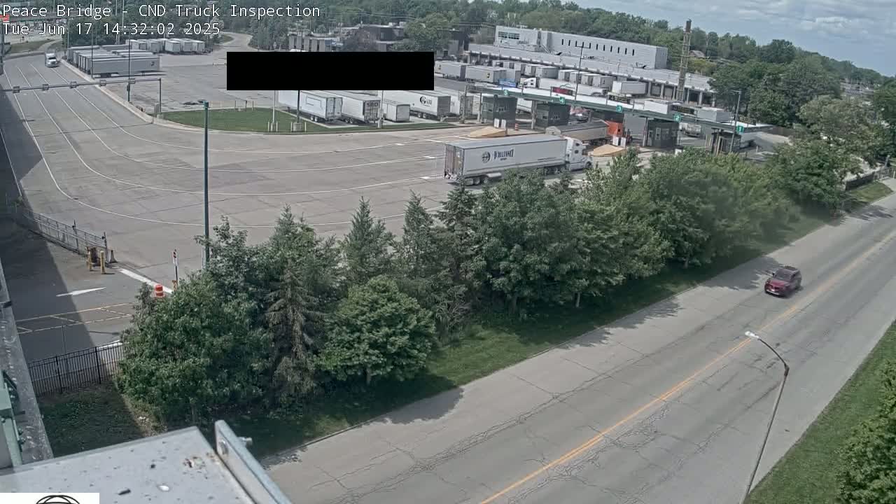 An aerial view of a truck inspection station on a partly cloudy day, showing several trucks in the lot and a car on a nearby road.