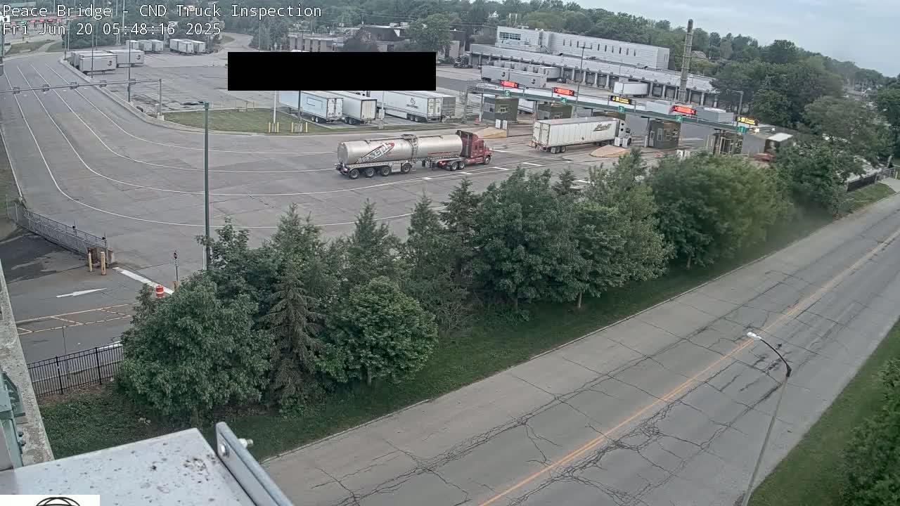 An overhead view shows a truck inspection station with several trucks, surrounded by green trees under an overcast sky.