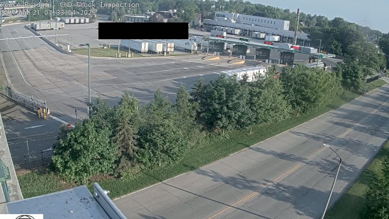 A high-angle view shows a truck inspection station with several semi-trucks parked nearby, under a mostly sunny sky.