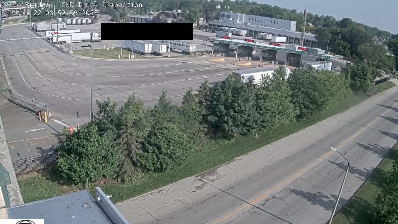 A sunny, outdoor view of a truck inspection station with several semi-trucks parked and a road leading away from it.
