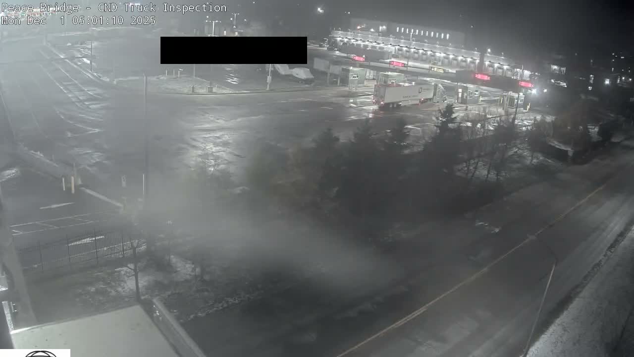A nighttime view depicts an illuminated truck inspection facility with multiple tractor-trailers on wet and possibly icy pavement, enveloped in a foggy or misty atmosphere.