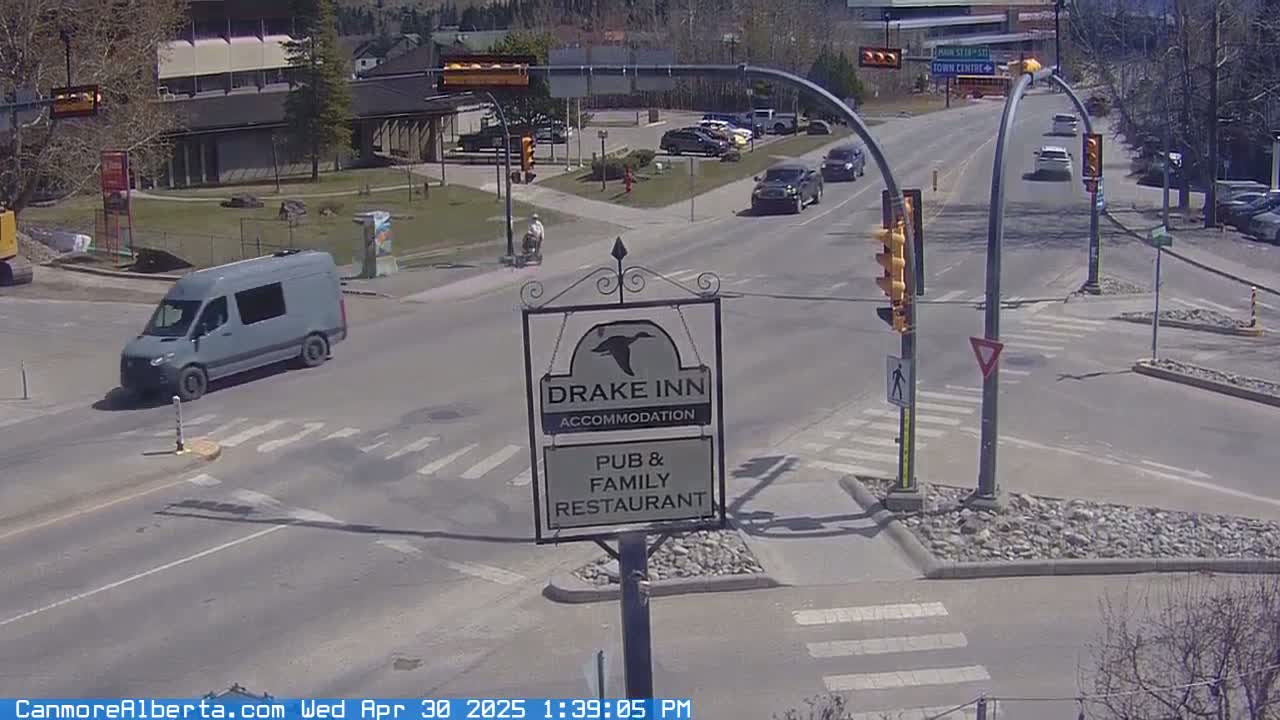 A gray van is parked near a four-way intersection on a sunny day, with several other vehicles visible on the road.