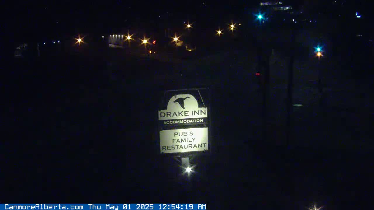 A nighttime view shows a Drake Inn sign illuminated in front of a dark, sparsely lit area.