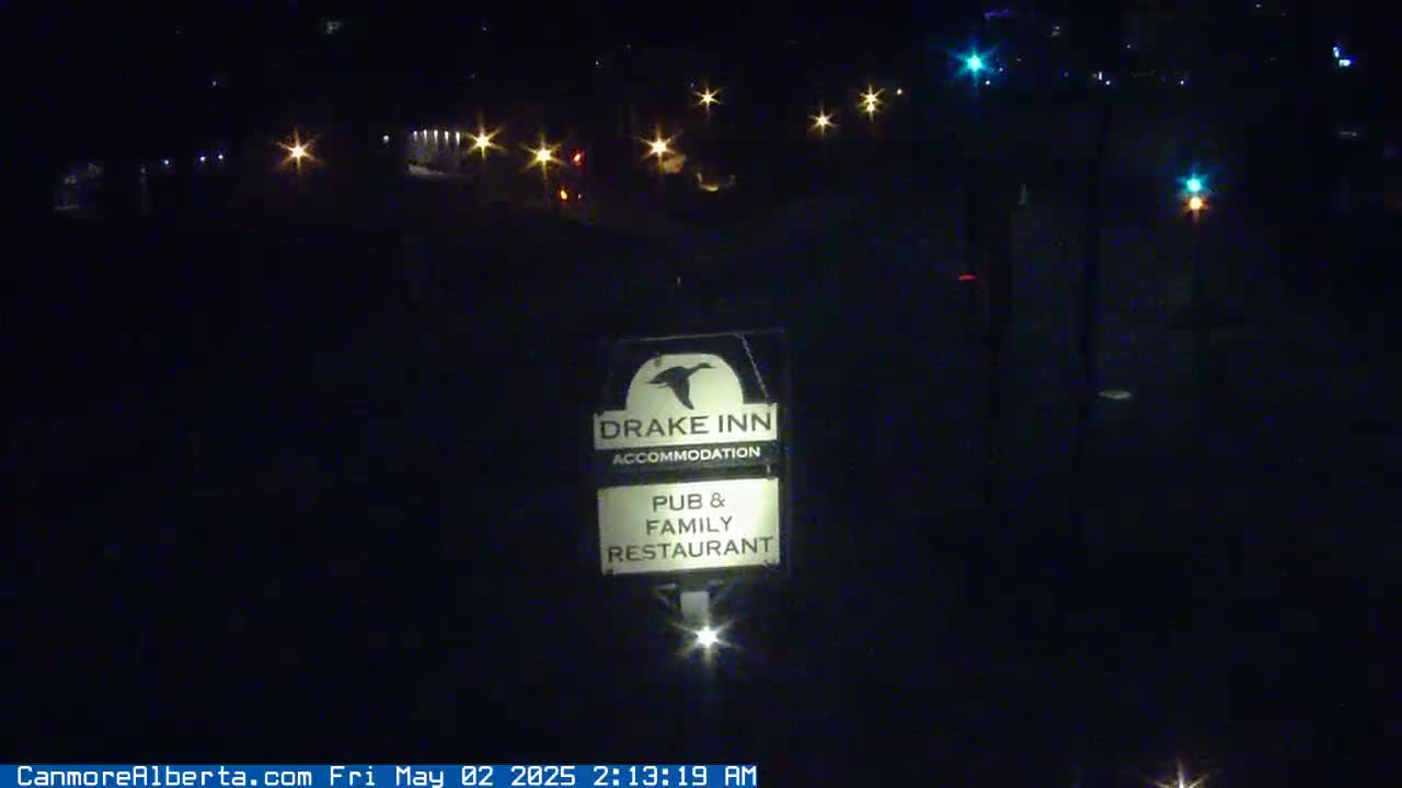 A nighttime view of a Drake Inn sign, illuminated by distant lights, under a dark, clear sky.