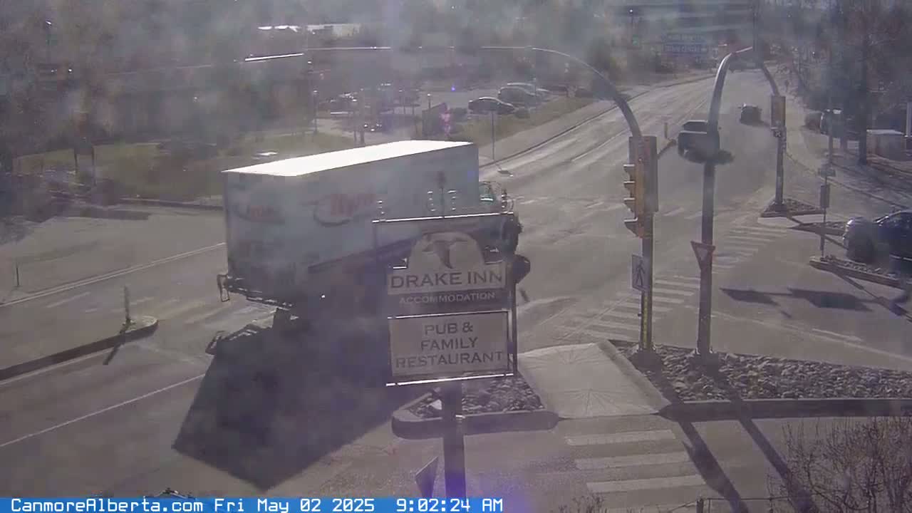 A large white truck is stopped at a road intersection on a sunny day, with several cars visible in the background.