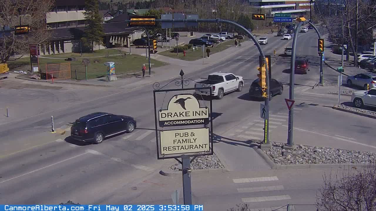 A sunny street intersection shows several vehicles at a stop, with a Drake Inn pub and family restaurant sign visible.