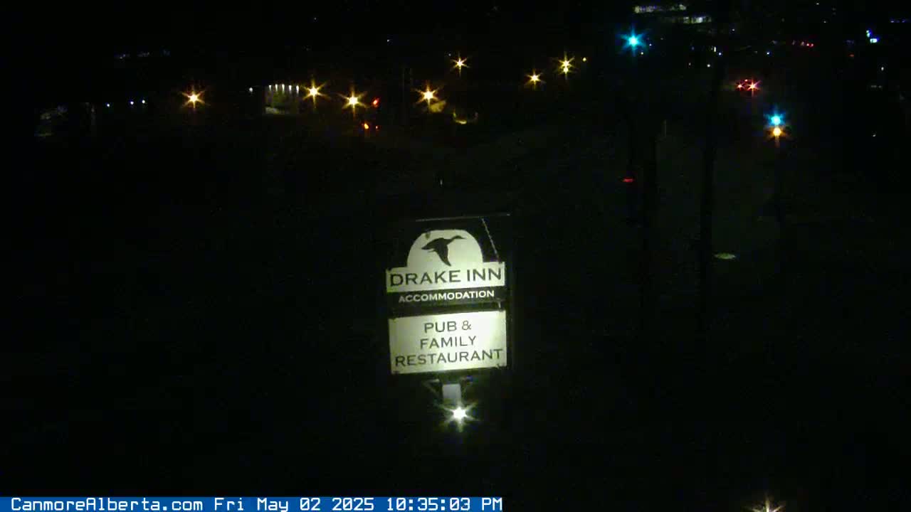 A nighttime view of a Drake Inn sign illuminated by a light source, showing distant car lights in the background.