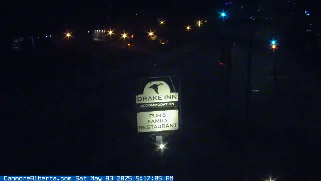 A nighttime view of a Drake Inn sign, illuminated against a dark background with distant lights and a road visible.