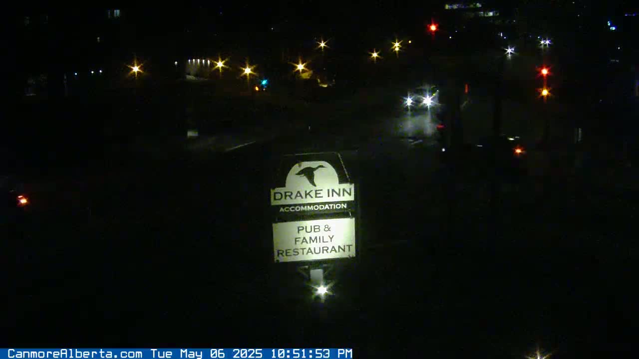 A nighttime view of a Drake Inn sign, illuminated by its own light and the distant lights of vehicles and buildings.