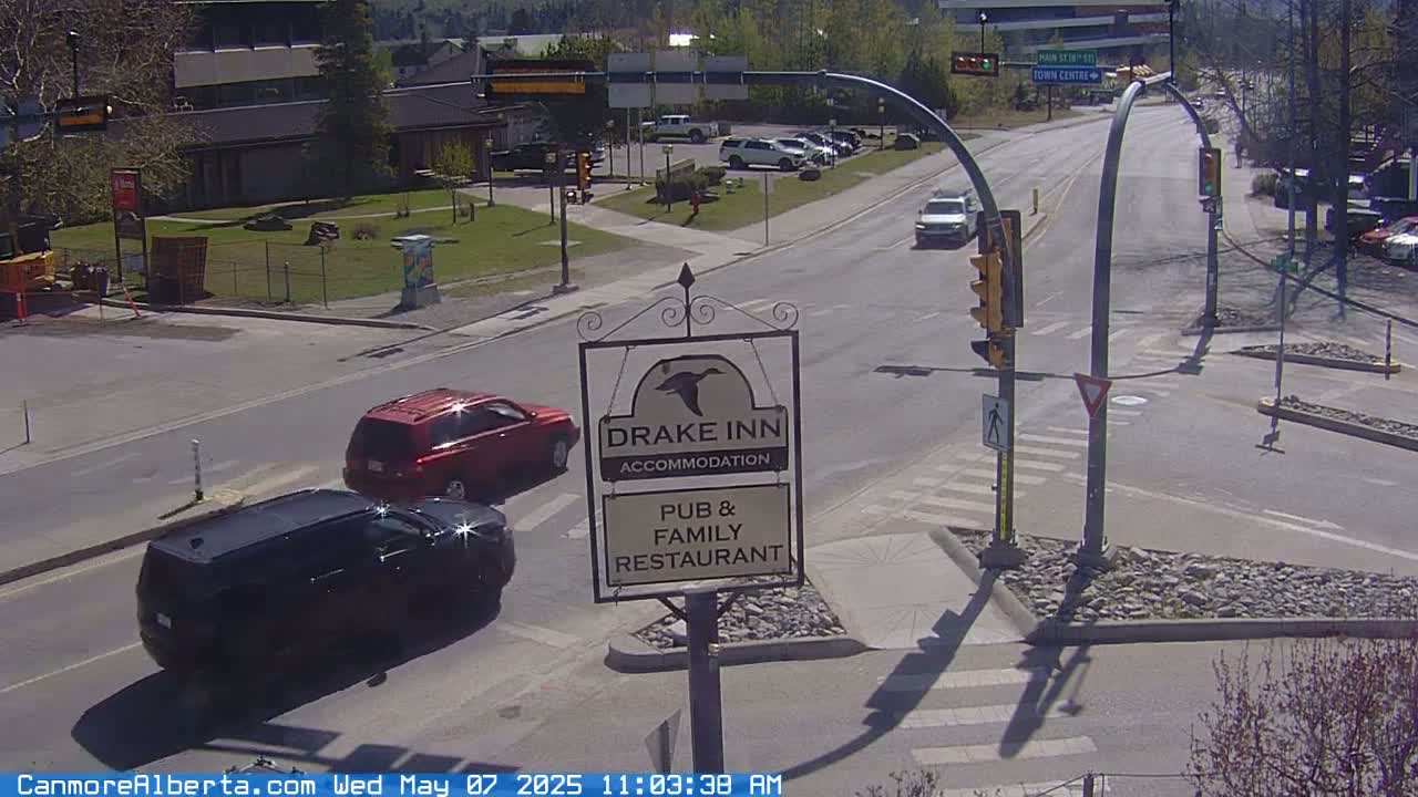 A sunny day shows a street intersection with two dark-colored SUVs and a red SUV, along with a Drake Inn sign.