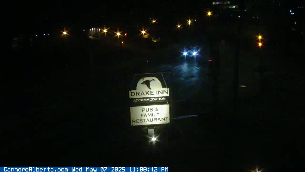 A nighttime view of a Drake Inn sign illuminated in the rain, with distant vehicle headlights visible.