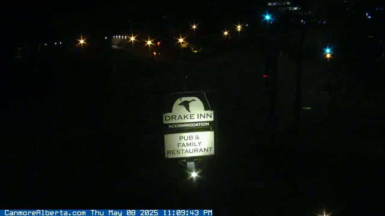 A nighttime view of a Drake Inn sign, illuminated, with distant streetlights visible in the dark.