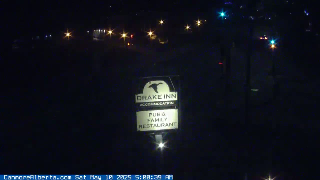 At night, a Drake Inn sign illuminated by a light, shows it's a pub and family restaurant with accommodation, while distant vehicle lights are visible in the dark.