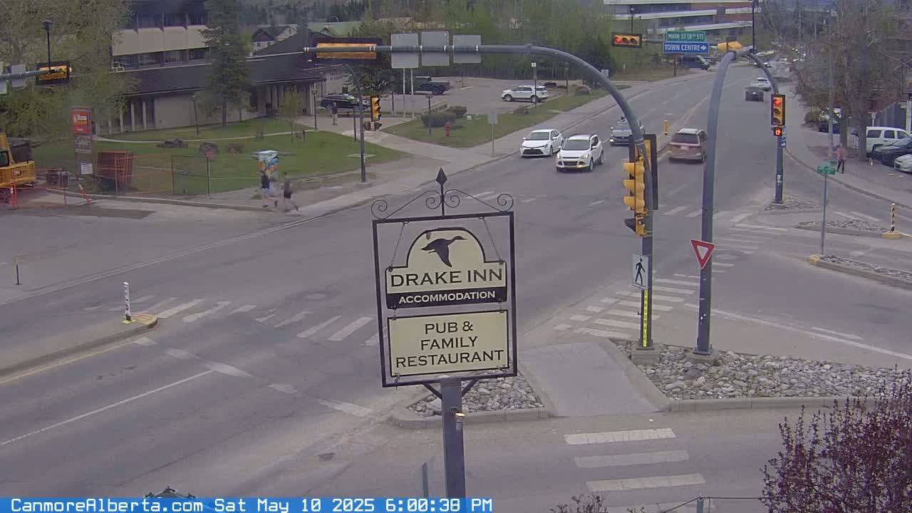 A street intersection with several cars, pedestrians, and a Drake Inn sign, under an overcast sky.