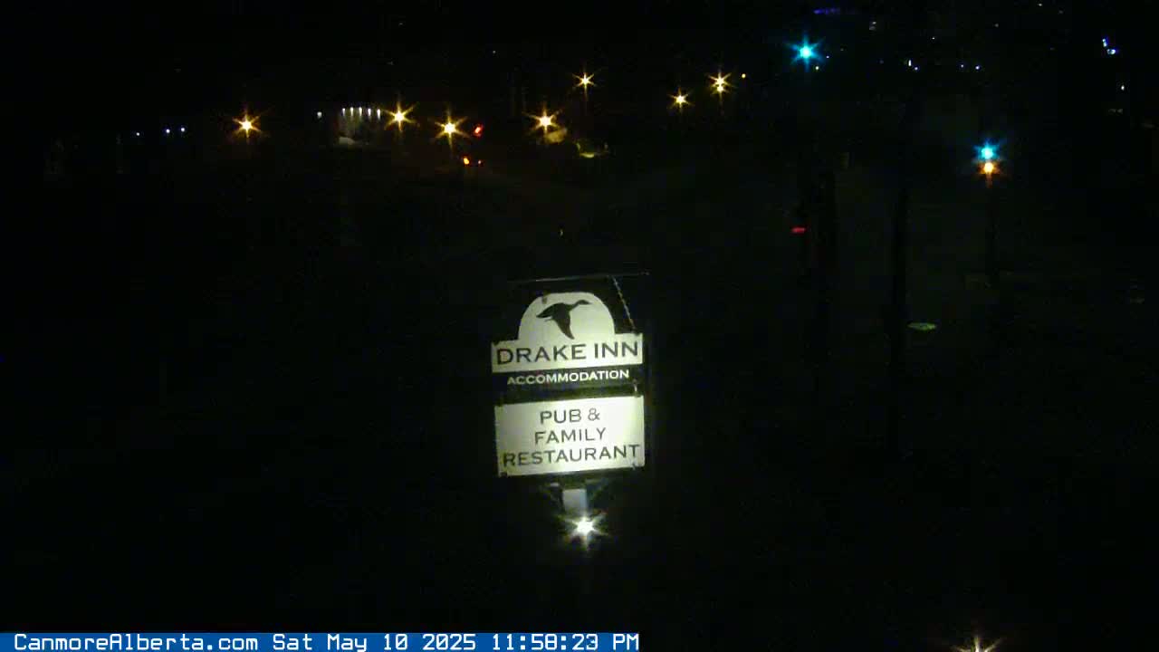 A nighttime outdoor scene shows a Drake Inn sign illuminated by a light source, with distant streetlights visible in the dark.