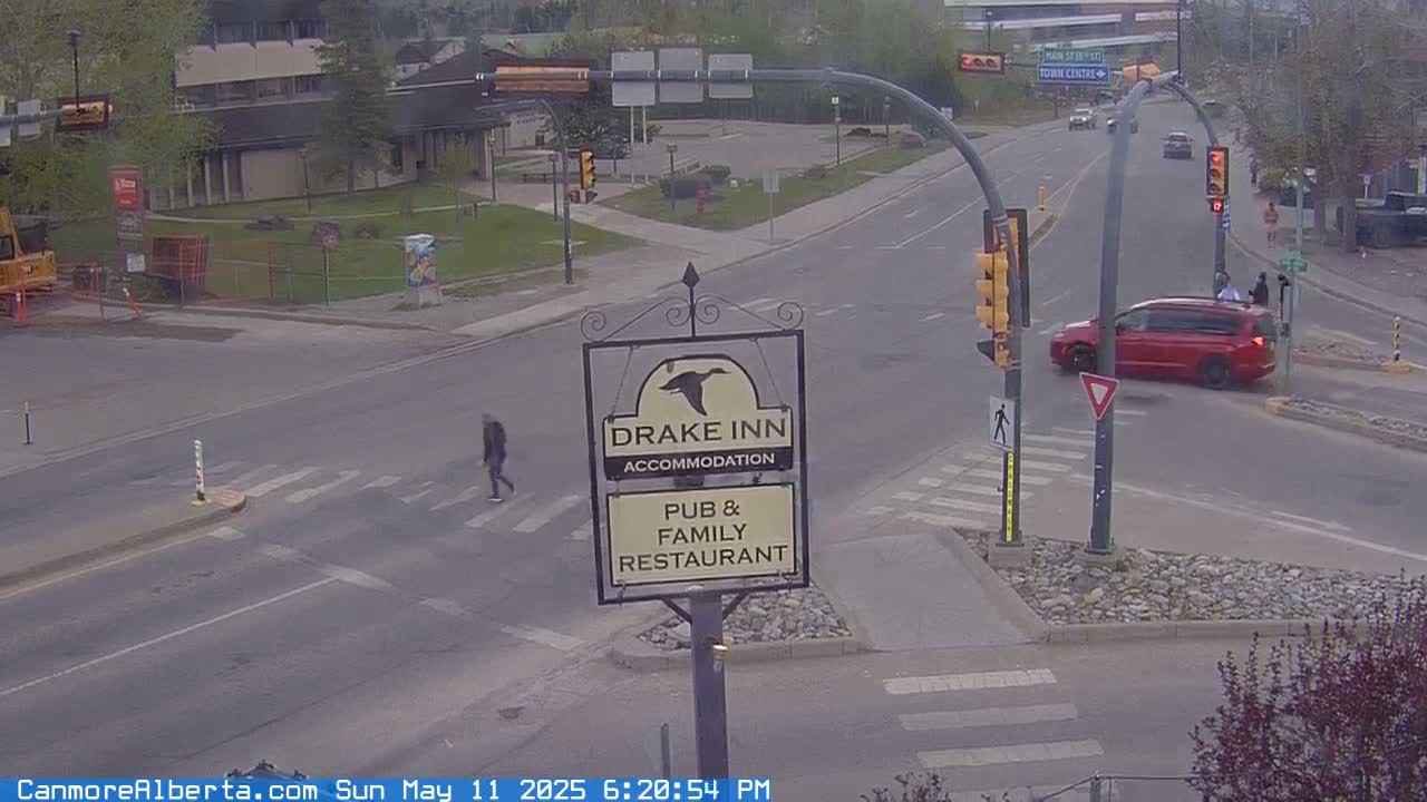 A partly cloudy day shows a street intersection with a red minivan turning, a pedestrian crossing, and a Drake Inn sign.