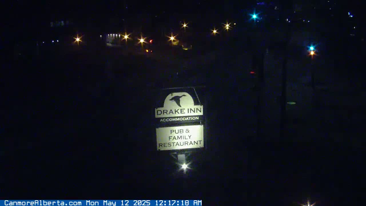A nighttime, outdoor view of a Drake Inn sign illuminated by a light source, with several distant car lights visible in the background.