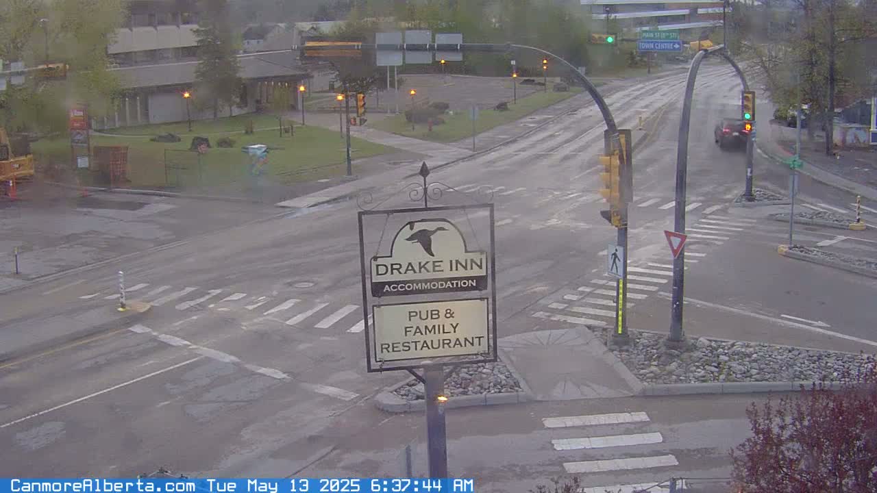 A wet, overcast street intersection shows a Drake Inn sign, a few cars, and buildings in the background.