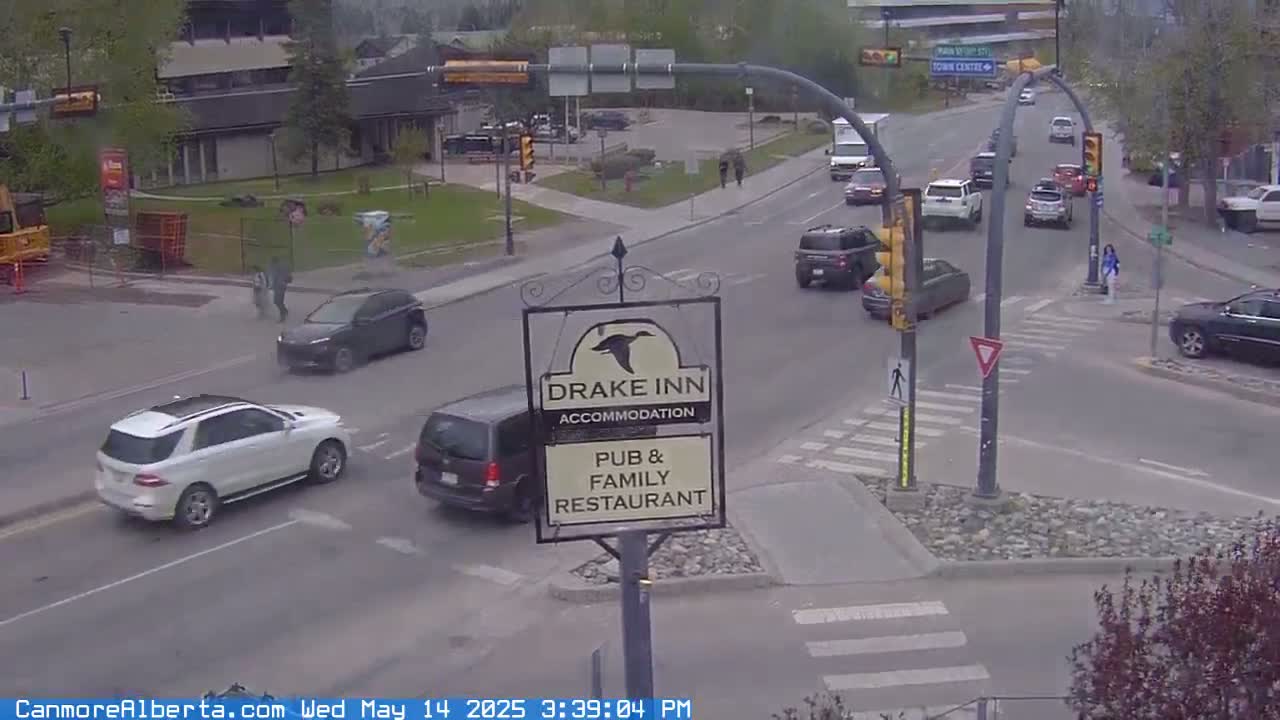 A street intersection with several cars, pedestrians, and a Drake Inn sign is shown on an overcast day.