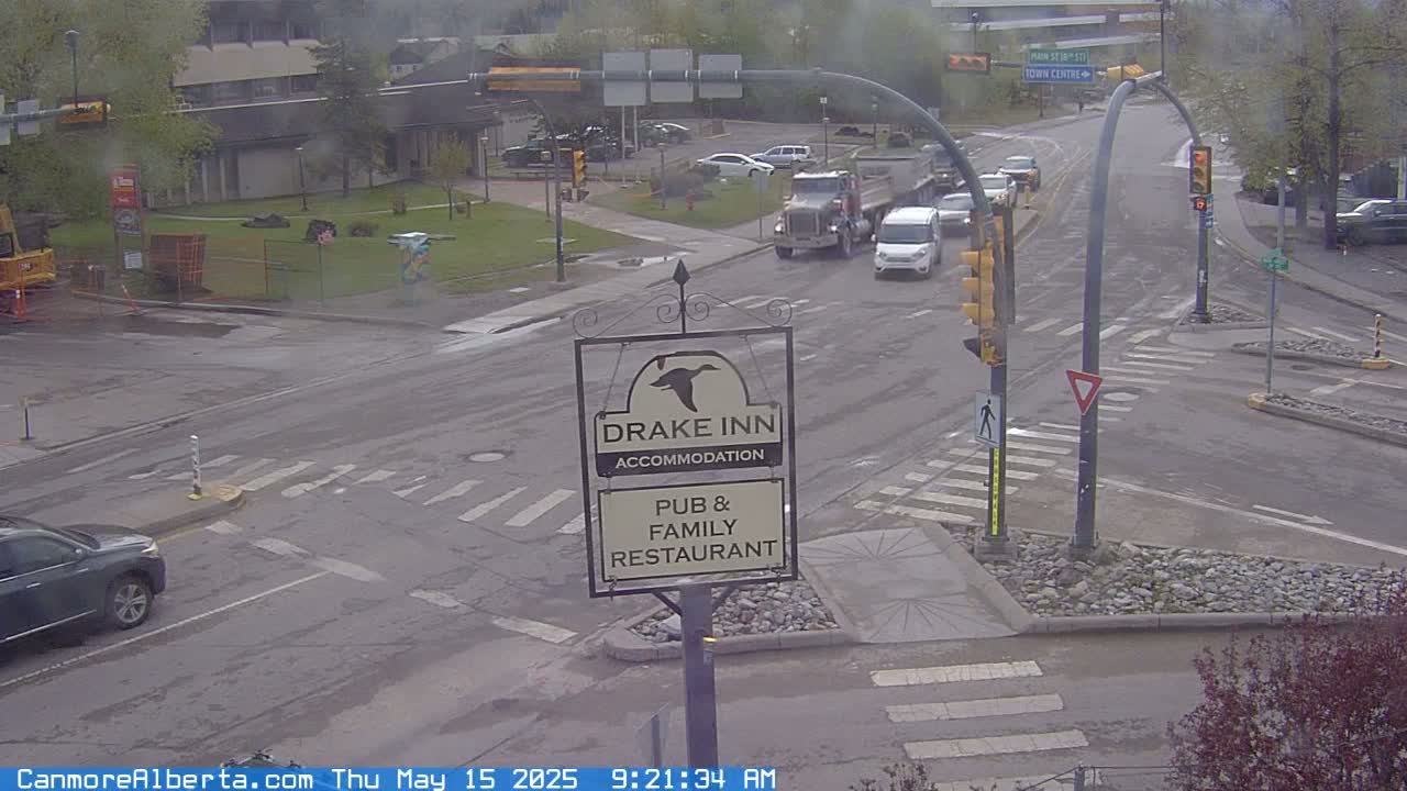 A wet street intersection with several vehicles, including a truck, and a Drake Inn sign is visible on an overcast day.