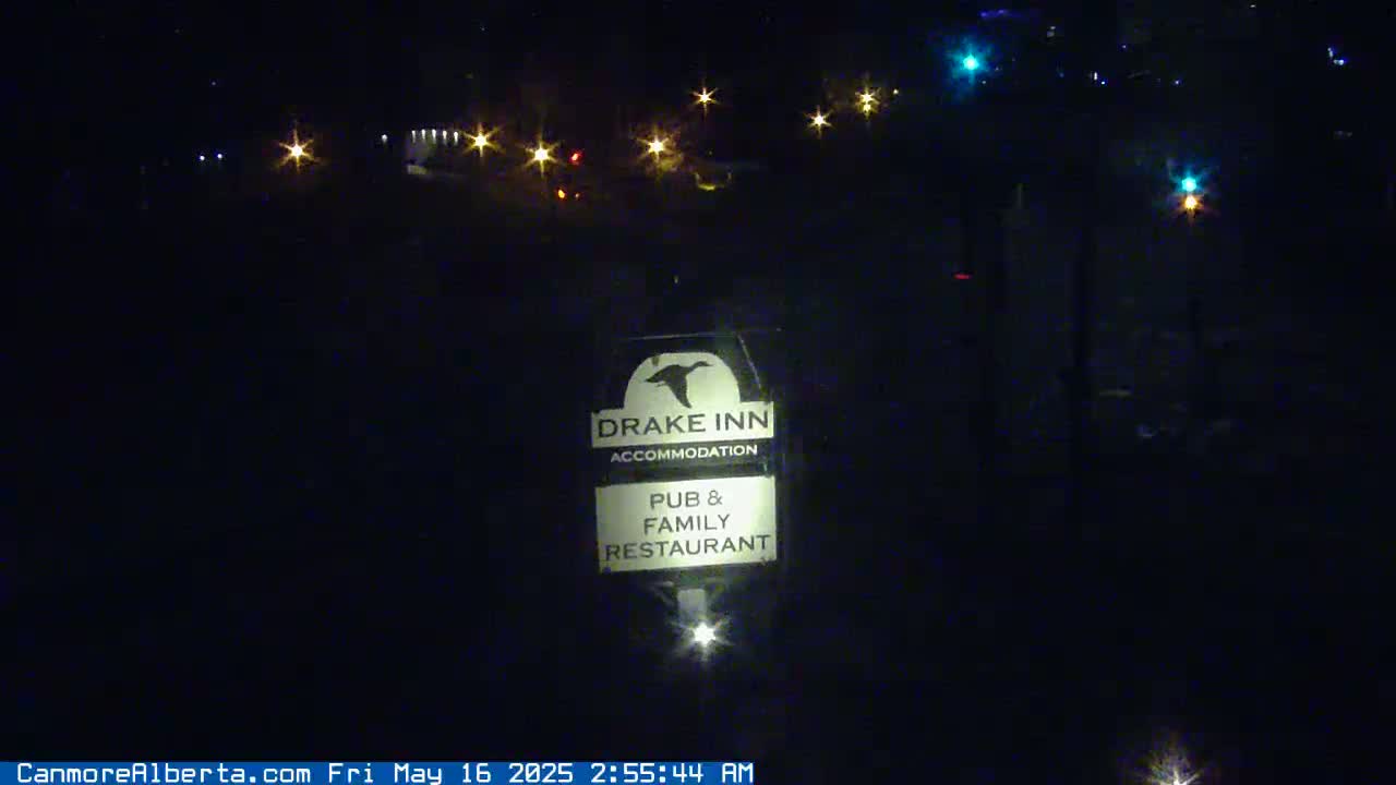A nighttime, outdoor view shows a Drake Inn sign illuminated in the dark, with distant lights suggesting a road or town in the background.