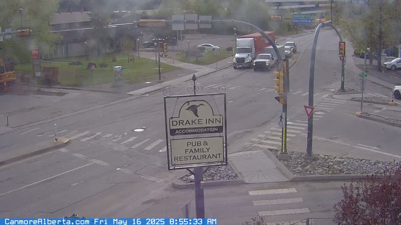 A street intersection on an overcast day shows several vehicles, including two semi-trucks, at a standstill, near a Drake Inn sign.