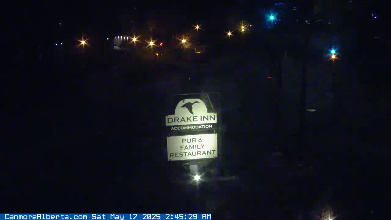 A nighttime, outdoor view shows a Drake Inn sign illuminated, with distant lights visible in the background.