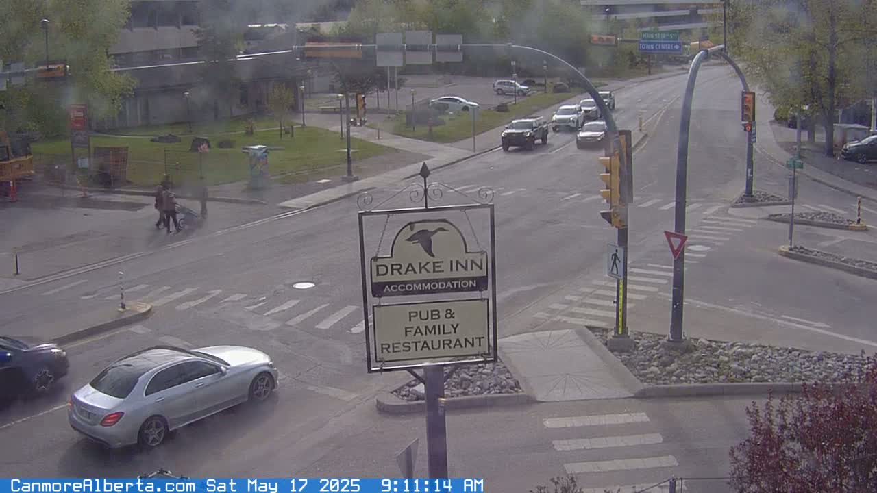 A street intersection with several cars, pedestrians, and a Drake Inn sign is visible on an overcast day.