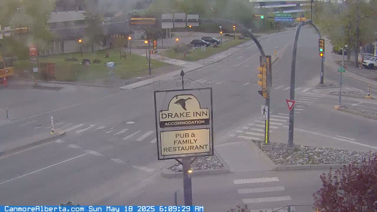 A hazy, overcast scene shows a street intersection with a Drake Inn sign, traffic lights, and several parked cars.