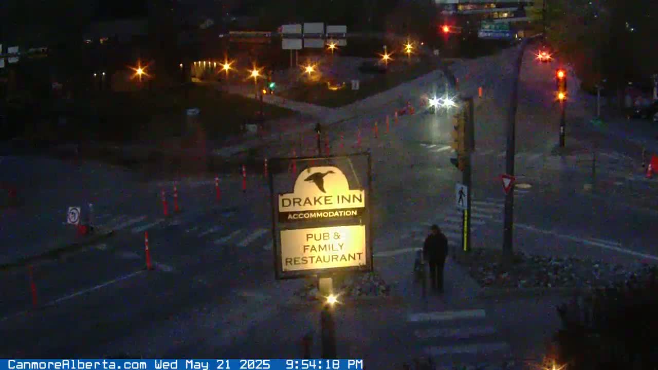 A nighttime view of a Drake Inn sign at a dimly lit intersection with some traffic and pedestrians, under dark conditions.