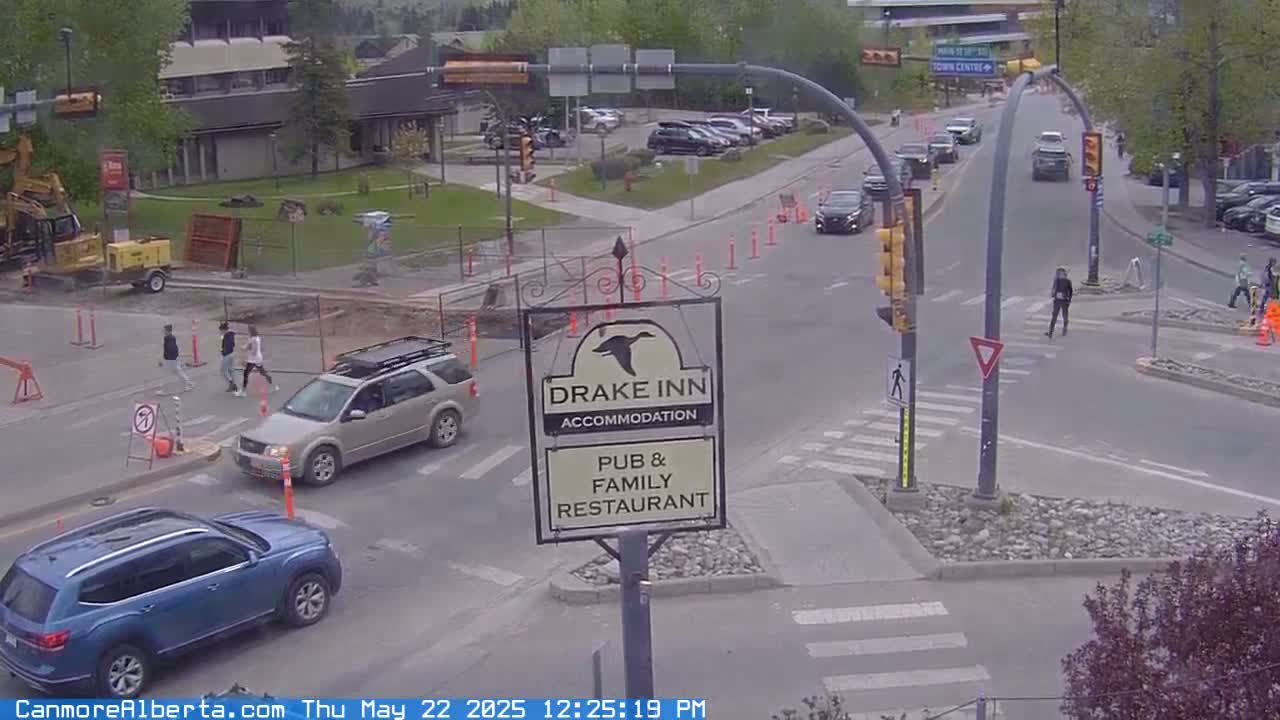 A street intersection with pedestrians and vehicles on a partly cloudy day, showing a Drake Inn sign.