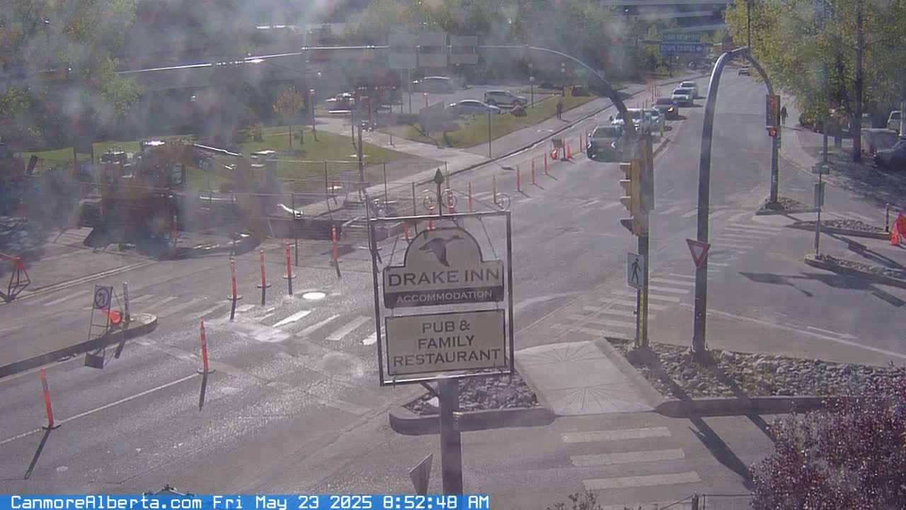 A sunny street scene shows a road intersection with some cars, construction equipment, and orange traffic cones, and a Drake Inn sign.