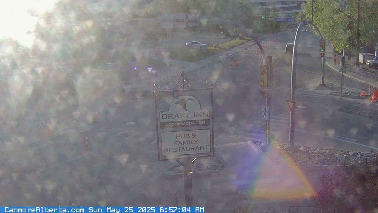 A hazy, sunny morning view shows a street intersection with a Drake Inn pub and family restaurant sign, a few cars, and pedestrians.