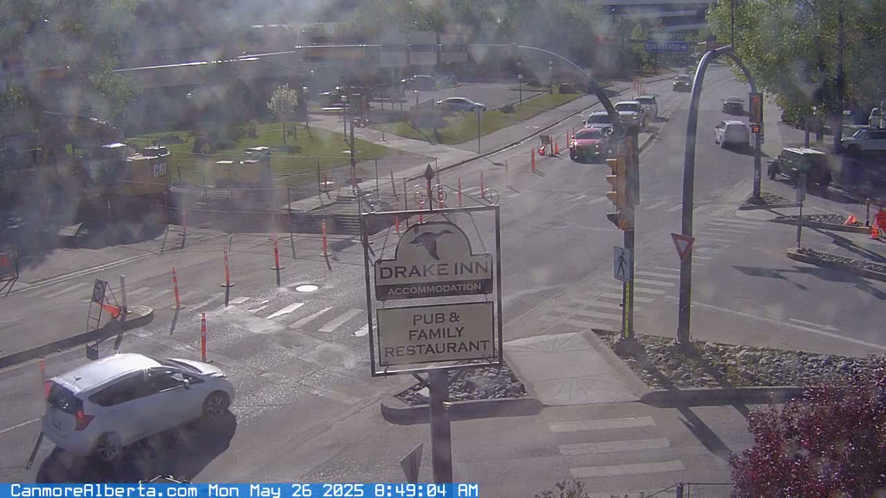 A sunny street scene shows a busy intersection with several vehicles, a construction zone, and a Drake Inn sign.