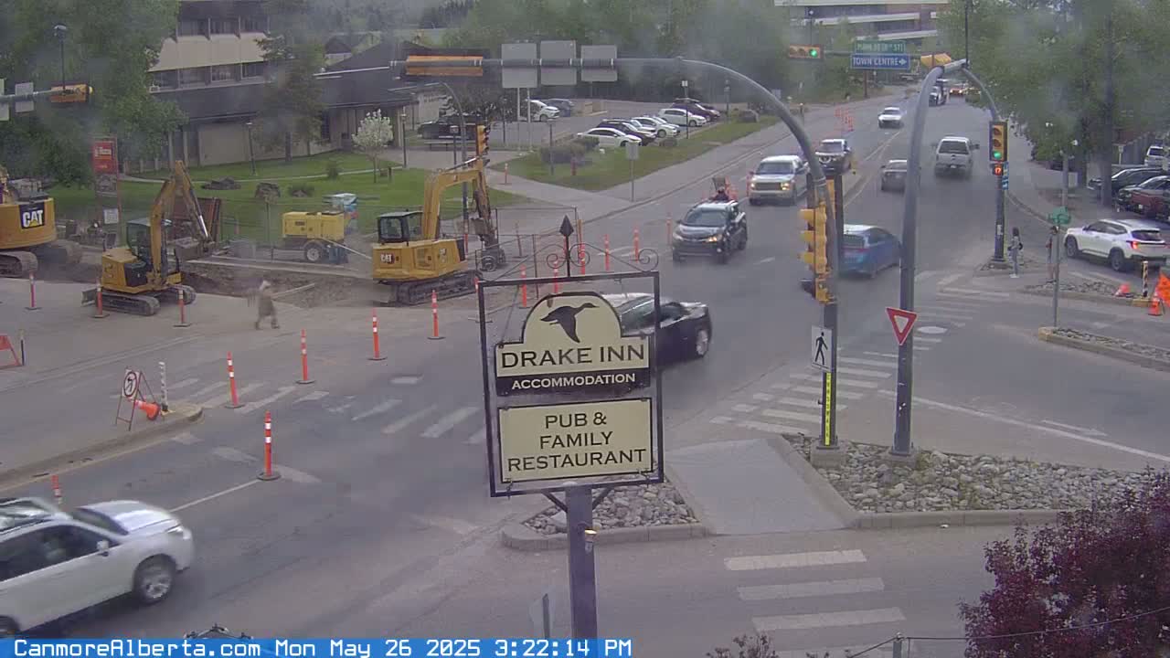 A street intersection with construction workers and several vehicles, under an overcast sky.