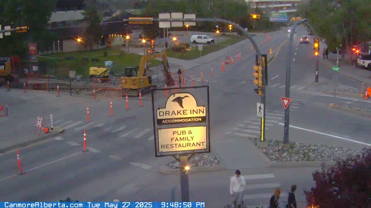 A street intersection at dusk with road construction, pedestrians, and vehicles, under overcast skies.