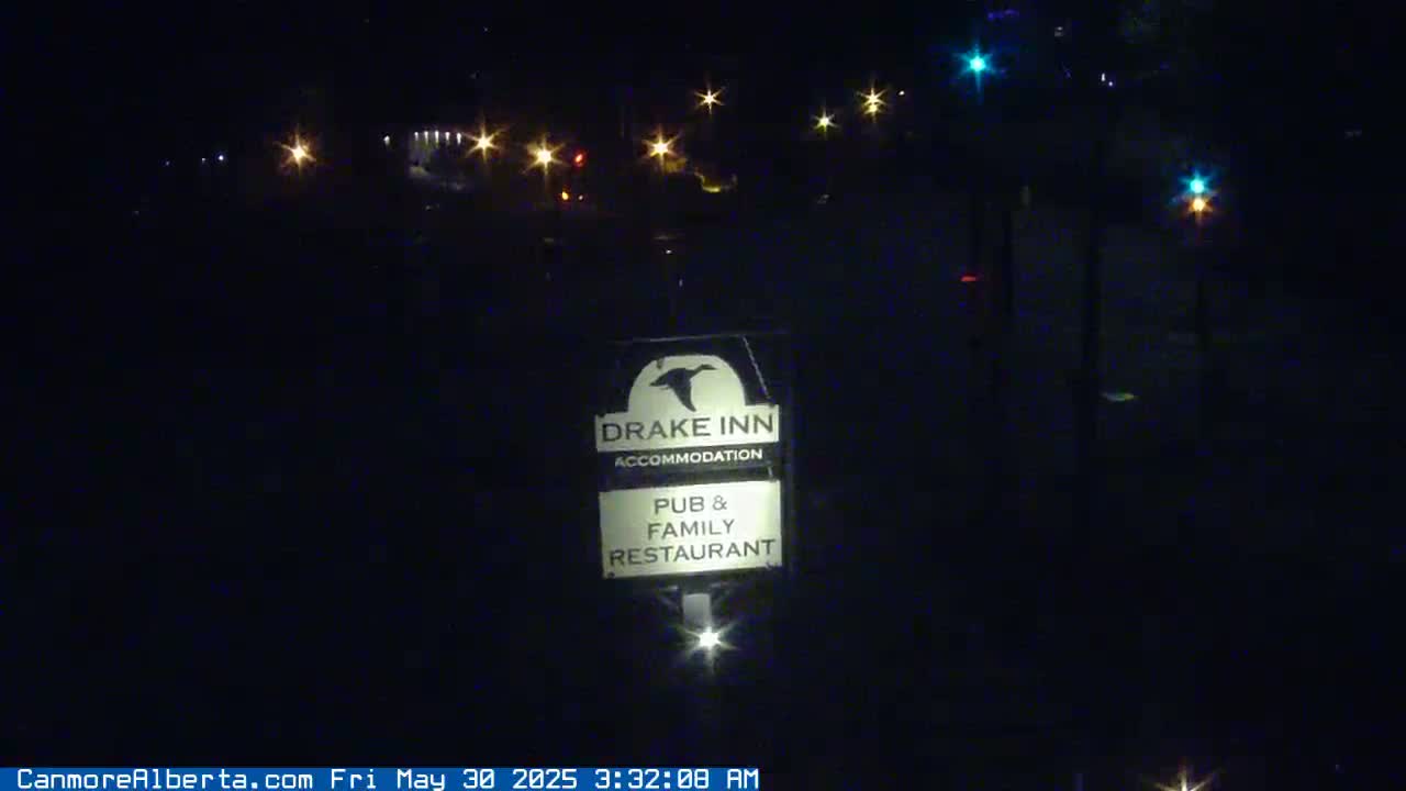 A nighttime image shows a Drake Inn sign illuminated in front of a dark, dimly lit area with several distant lights.